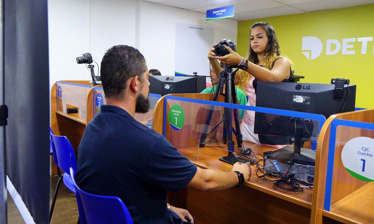 Funcionária do Detran atendendo homem, que tira foto para carteira de habilitação em Posto do Detran 