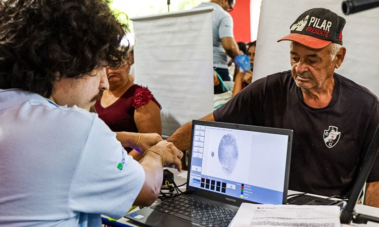 Funcionário do Detran atende idoso que cadastra as digitais para tirar carteira de identidade. Ao fundo uma mulher também é atendida.