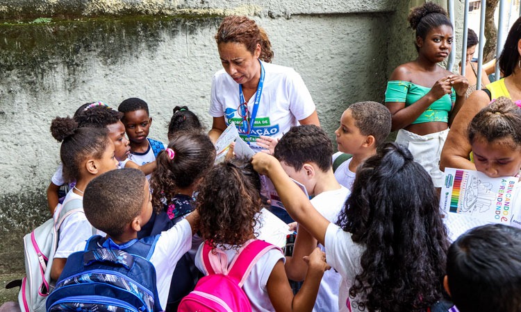 Funcionária do Detran entrega blocos de colorir em escola e está rodeada de crianças