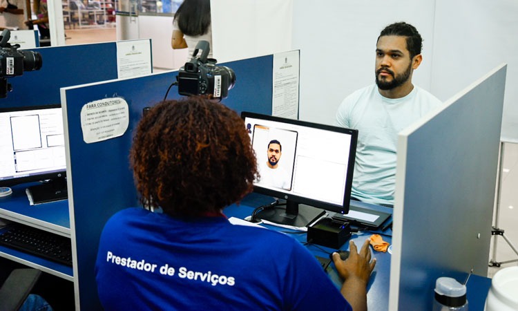 Funcionária do Detran atendendo homem, que tira foto para habilitação em Posto do Detran 