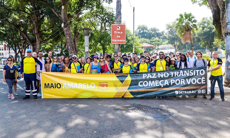 grupo de aproximadamente 50 pessoas, posam para foto em evento de caminhada cultural com faixa do Maio Amarelo e paz no trânsito