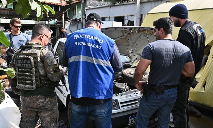 agentes de fiscalização do Detran com policiais civil e militar verificam motor de carro em ferro-velho