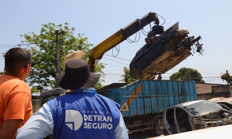 Agente do Detran observa operação com guindaste em ferro-velho