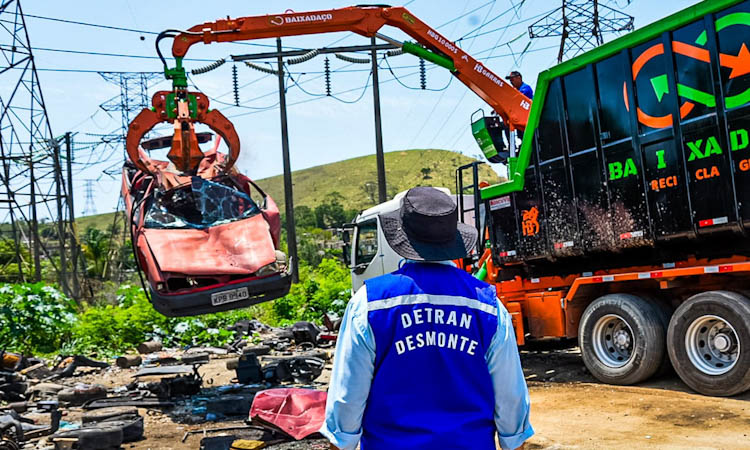agente de fiscalização do Detran observa carro suspenso por guindaste em ferro-velho