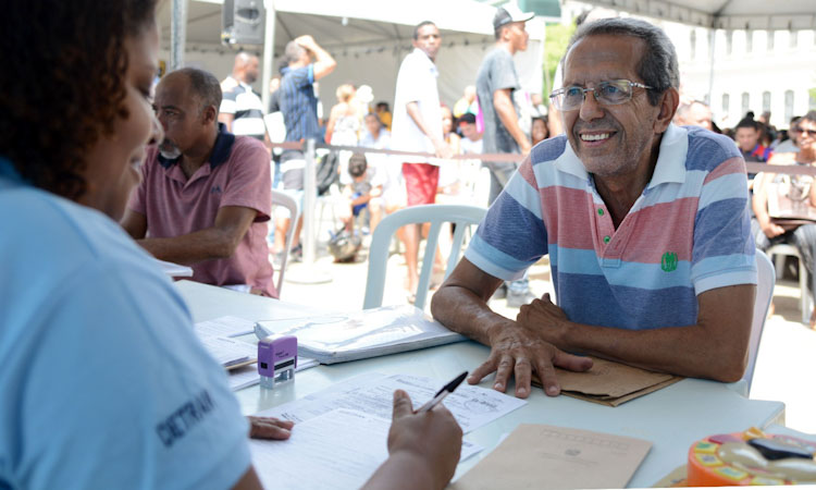 Usuário dos serviços do Detran, sorridente, é atendido por funcionária em unidade 