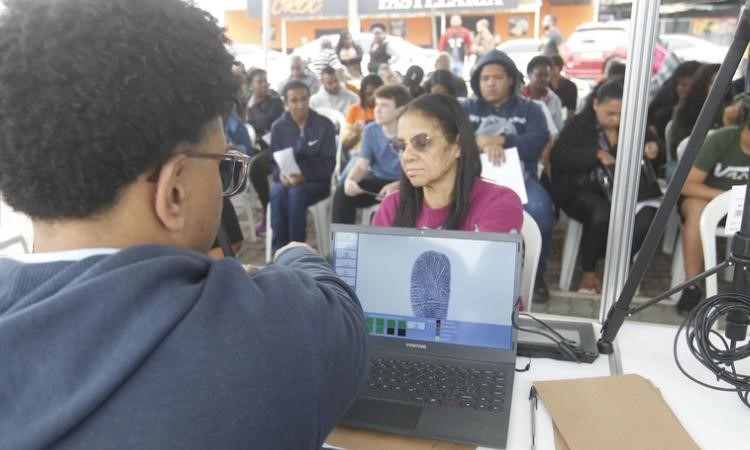 Funcionário do Detran presente tira as impressões digitais de uma mulher durante o Detran Presente em Três Rios. Na tela aparece a digital