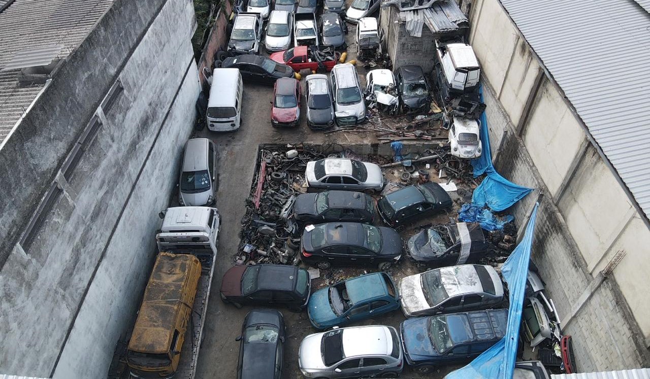 Vista aérea do pátio do ferro-velho, com dezenas de veículos e sucatas de veículos