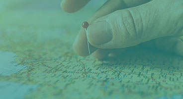 mão fincando um alfinete de cabeça vermelha em um mapa